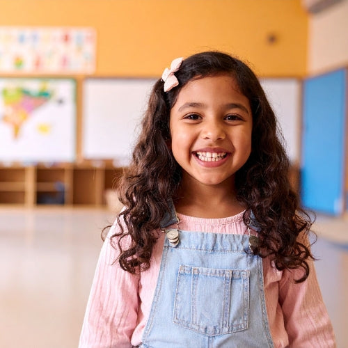 Young girl with a flower in her hair smiling in a classroom setting